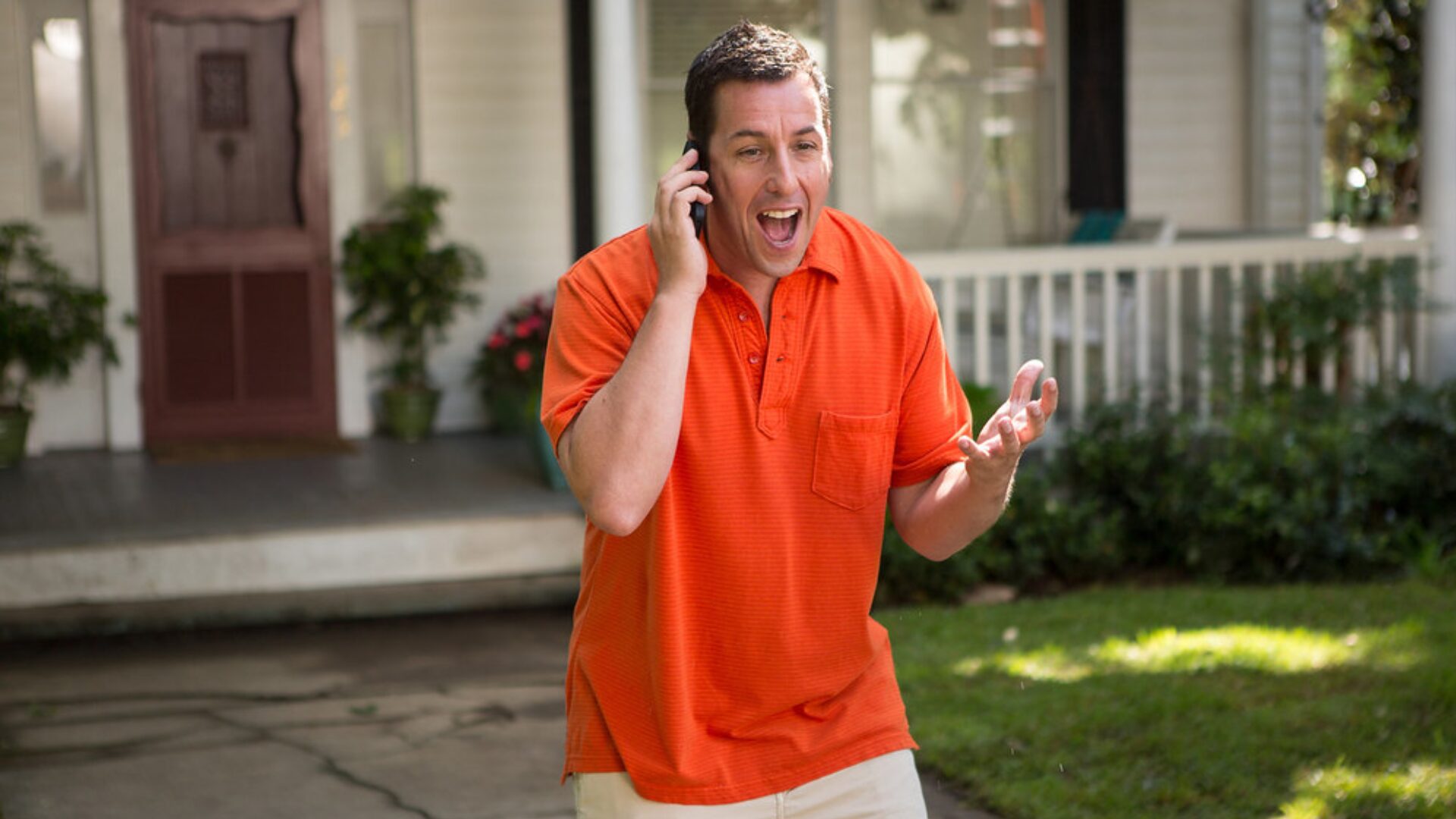 imagem onde ele esta atuando em algum filme, ele esta em frente a uma casa branca estadunidense com uma camiseta laranja e esta em uma ligação com cara de surpresa e felicidade