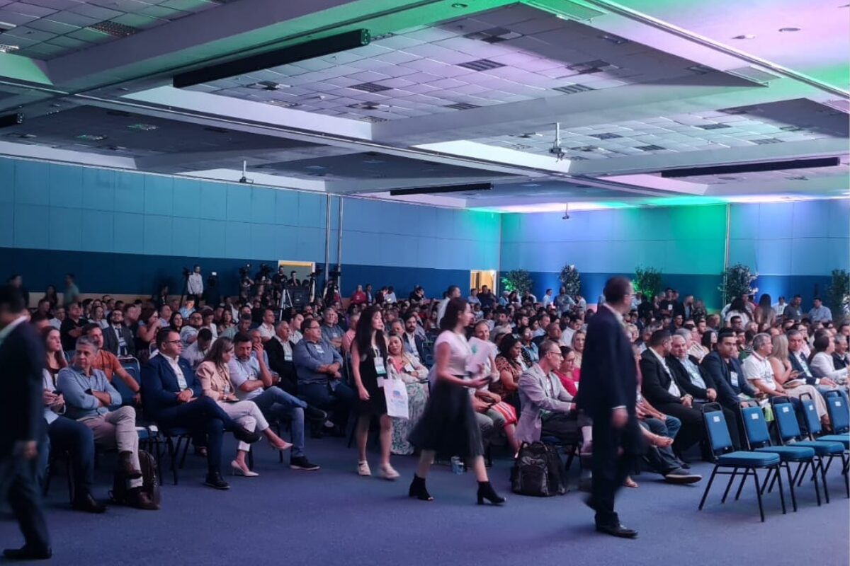 na imagem esta presente um monte de pessoas sentadas participando de um encontro de municípios paranaenses