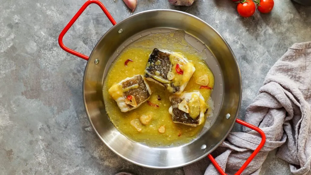 uma panela com um molho e tres pedaços de bacalhau