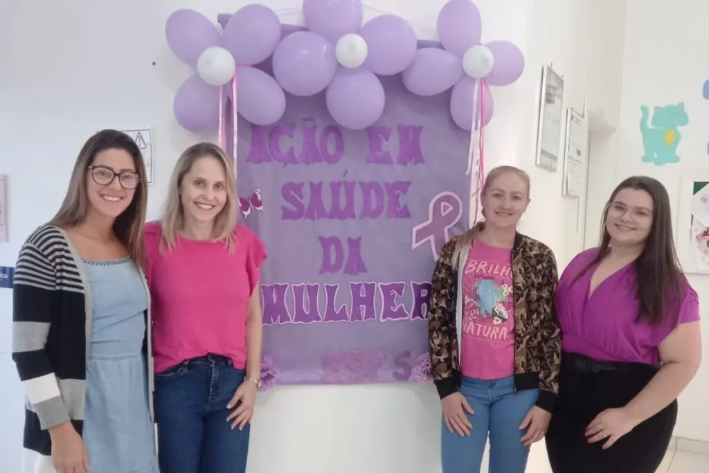 4 Mulheres da equipe do ESF 5 tirando foto com cartaz escrito "Ação em saúde da mulher"